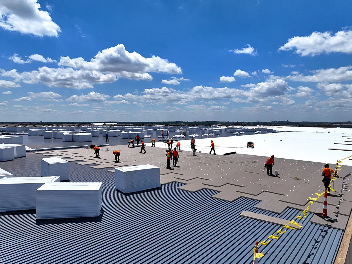 Crew staging insulation boards on a large warehouse's metal roof deck – TPO roofs project gallery