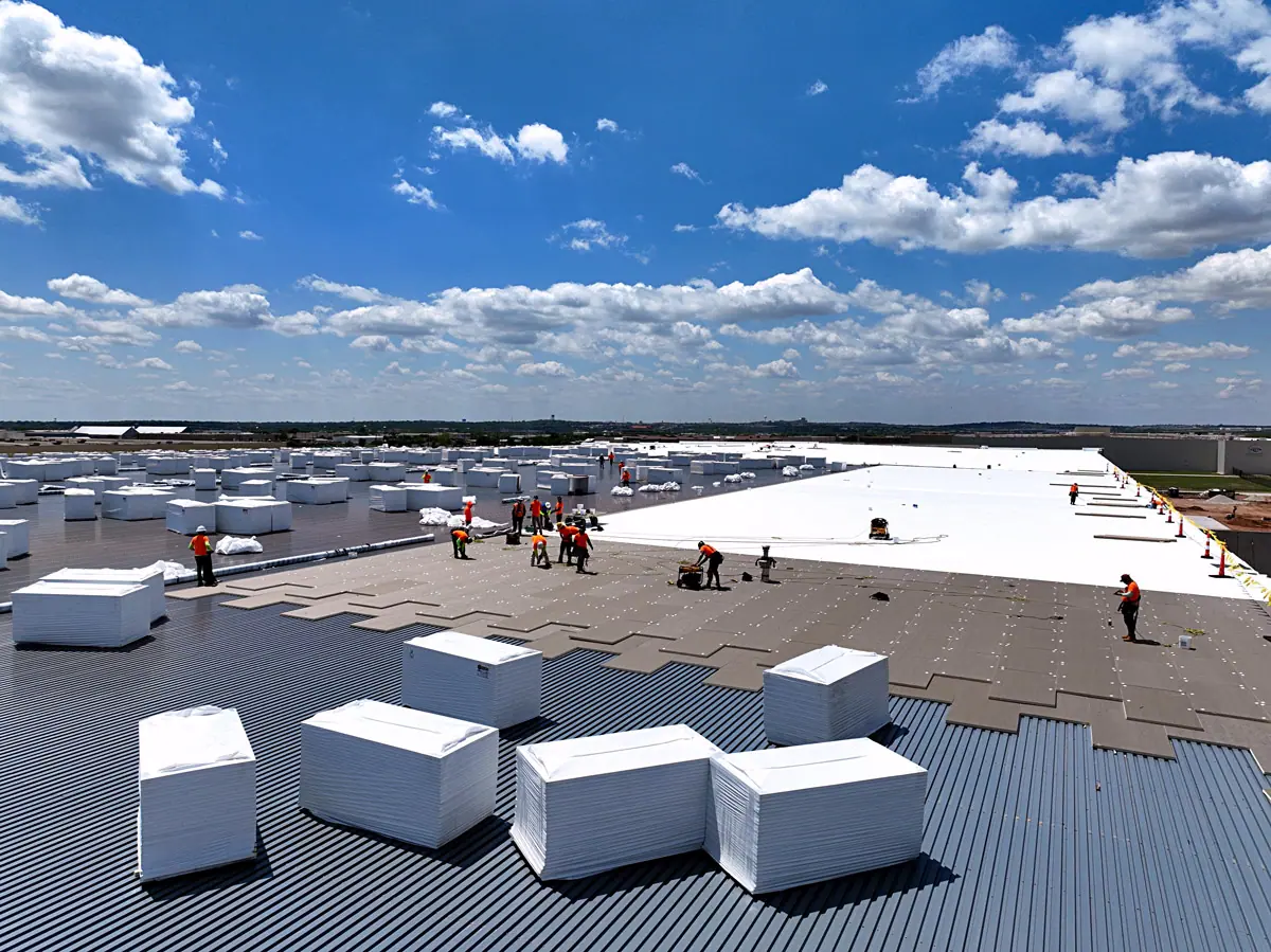 Crew staging insulation boards on a large warehouse's metal roof deck – TPO roofs project gallery