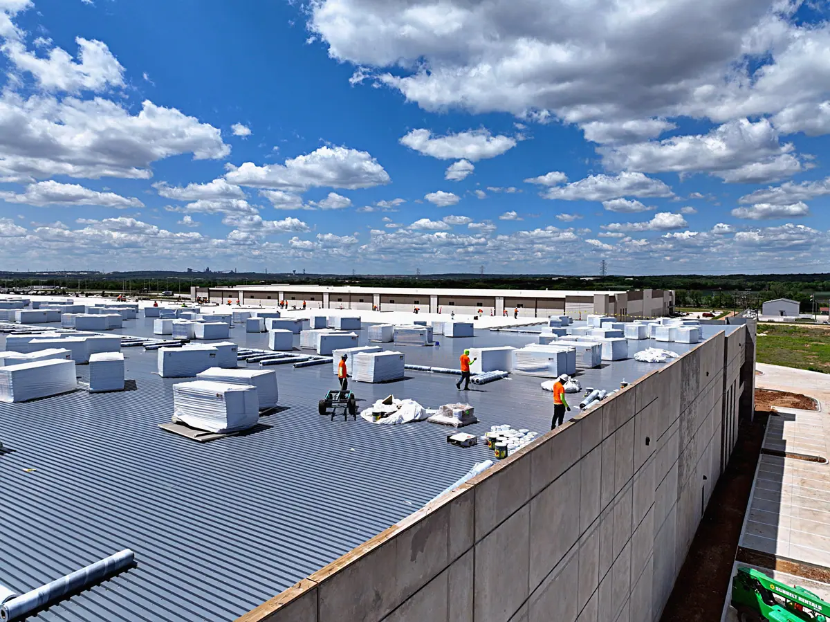Crew staging insulation boards on a large warehouse's metal roof deck – TPO roofs project gallery
