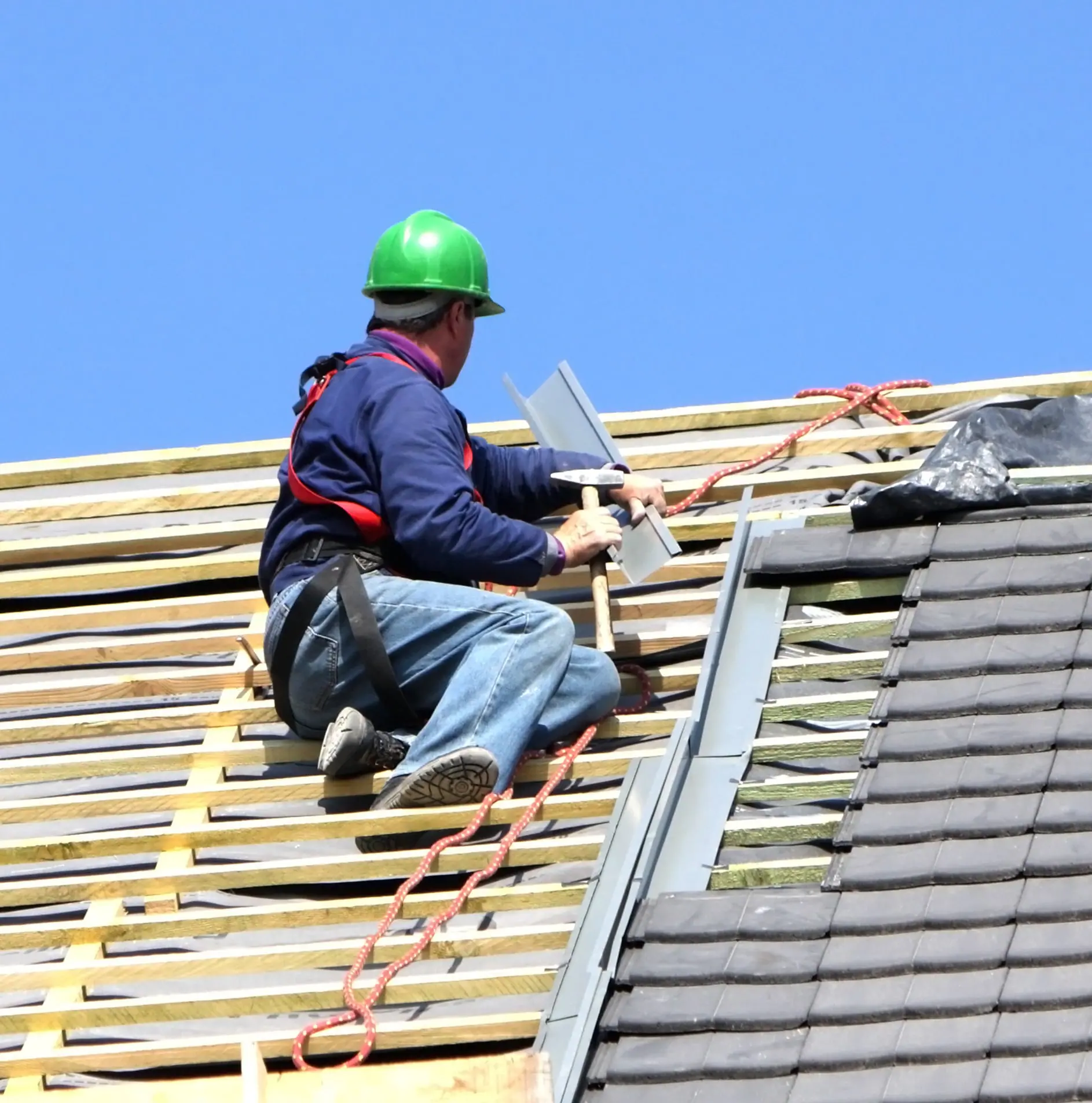 Roofer in a safety harness installing shingles on roof battens – Waco roofing company