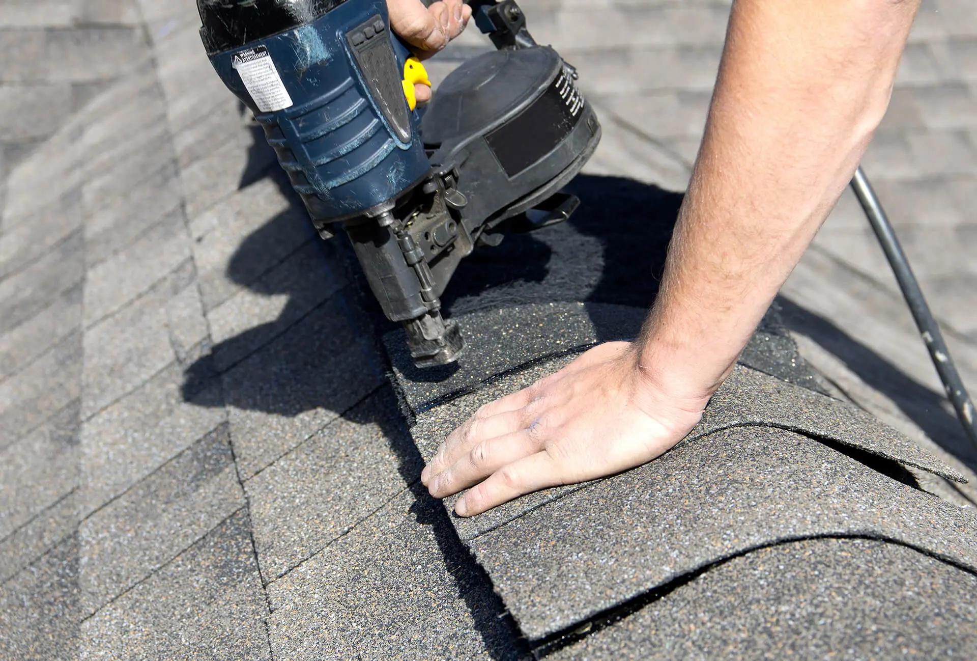 Roofer nailing down an asphalt shingle with a nail gun – roof types in Austin