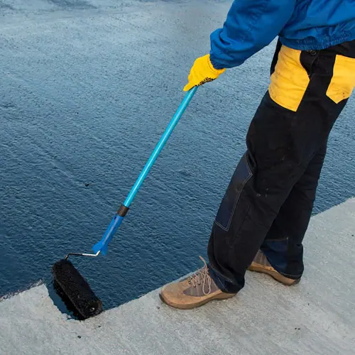 Worker rolling a coating onto a flat roof – roof types in Austin